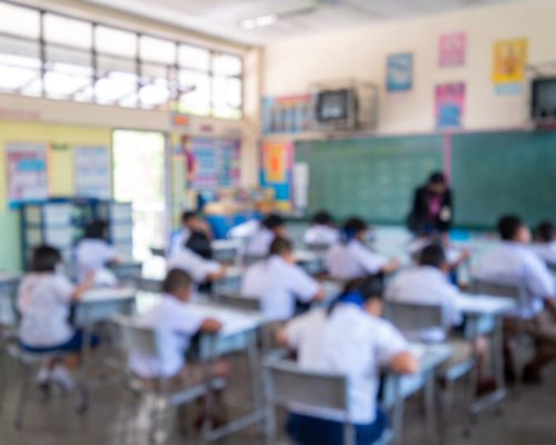 Education evaluation, Blurred image of Writing test in exam with behind child asian students group concentrate in primary school, final examination desk at classroom with Thai student uniform.