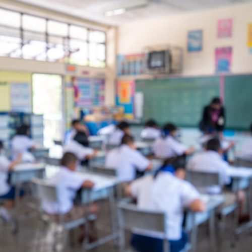 Education evaluation, Blurred image of Writing test in exam with behind child asian students group concentrate in primary school, final examination desk at classroom with Thai student uniform.