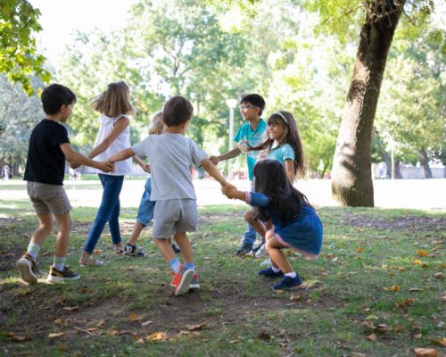 Happy children playing together outdoors, dancing around on grass, enjoying outdoor activities and having fun in park. Kids party or friendship concept