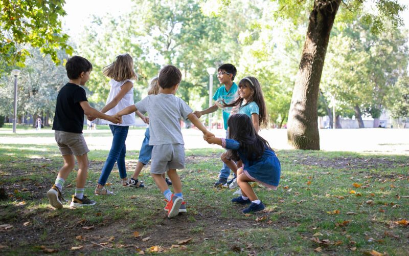 Happy children playing together outdoors, dancing around on grass, enjoying outdoor activities and having fun in park. Kids party or friendship concept