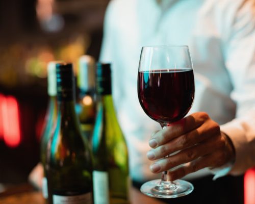 Mid section of bartender holding glass of red wine at bar counter