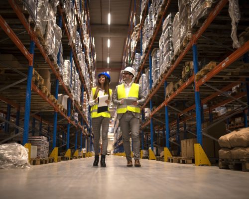 Managers walking through large warehouse controlling goods distribution.
