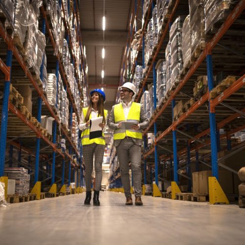 Managers walking through large warehouse controlling goods distribution.