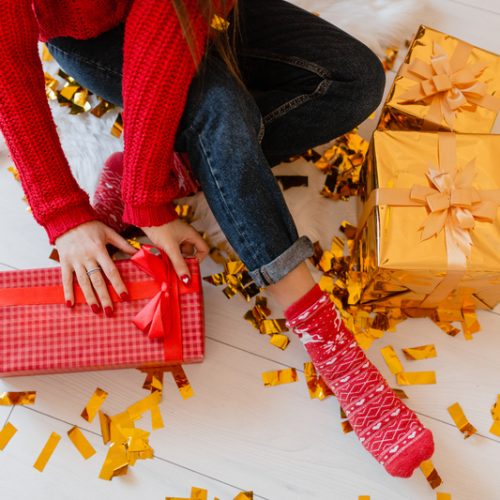view from above on woman in red socks sitting at home at christmas on golden confetti unpacking peresents and gift boxes