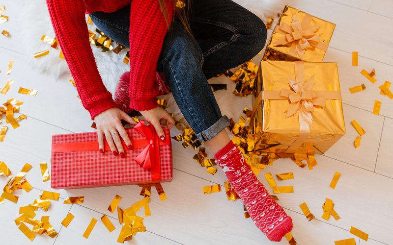 view from above on woman in red socks sitting at home at christmas on golden confetti unpacking peresents and gift boxes