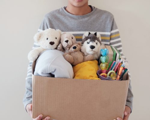 Young volunteer preteen teenage boy holding a box full of used toys, cloths, books and stationery for donation