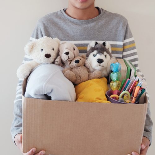 Young volunteer preteen teenage boy holding a box full of used toys, cloths, books and stationery for donation