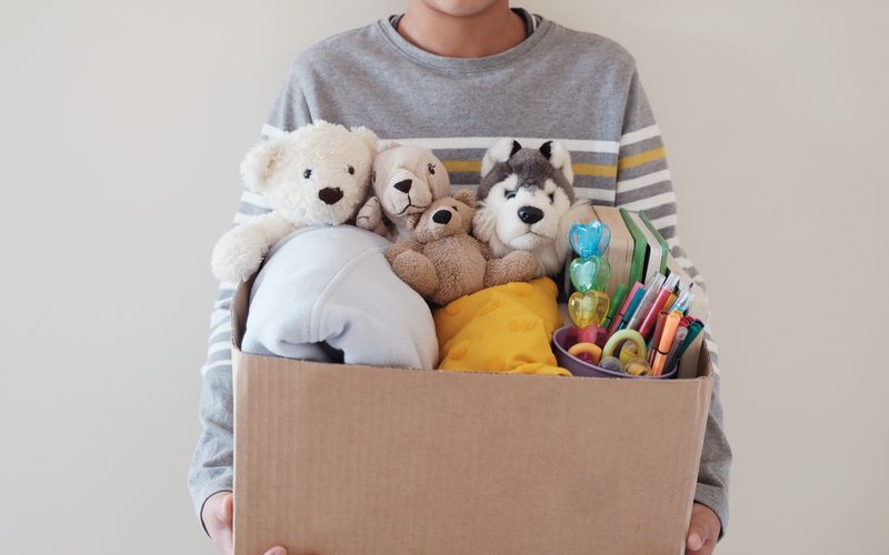 Young volunteer preteen teenage boy holding a box full of used toys, cloths, books and stationery for donation